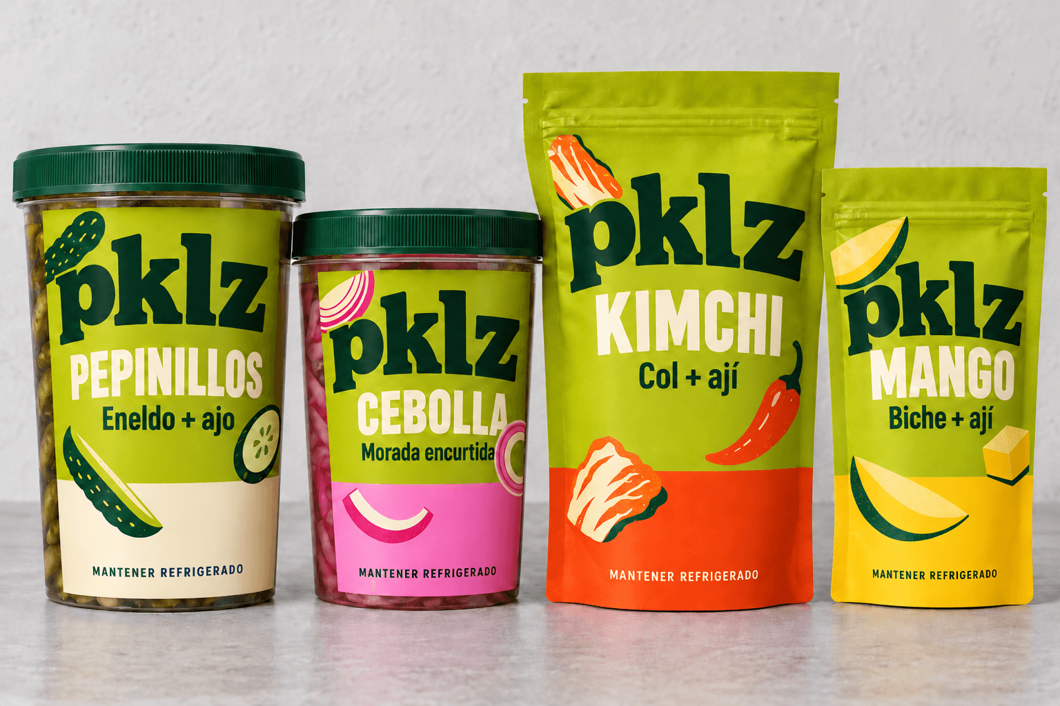 Los cuatro empaques pklz sobre una mesa: pepinillos, cebolla, kimchi y mango, todos con fondo lima y una banda de color abajo.